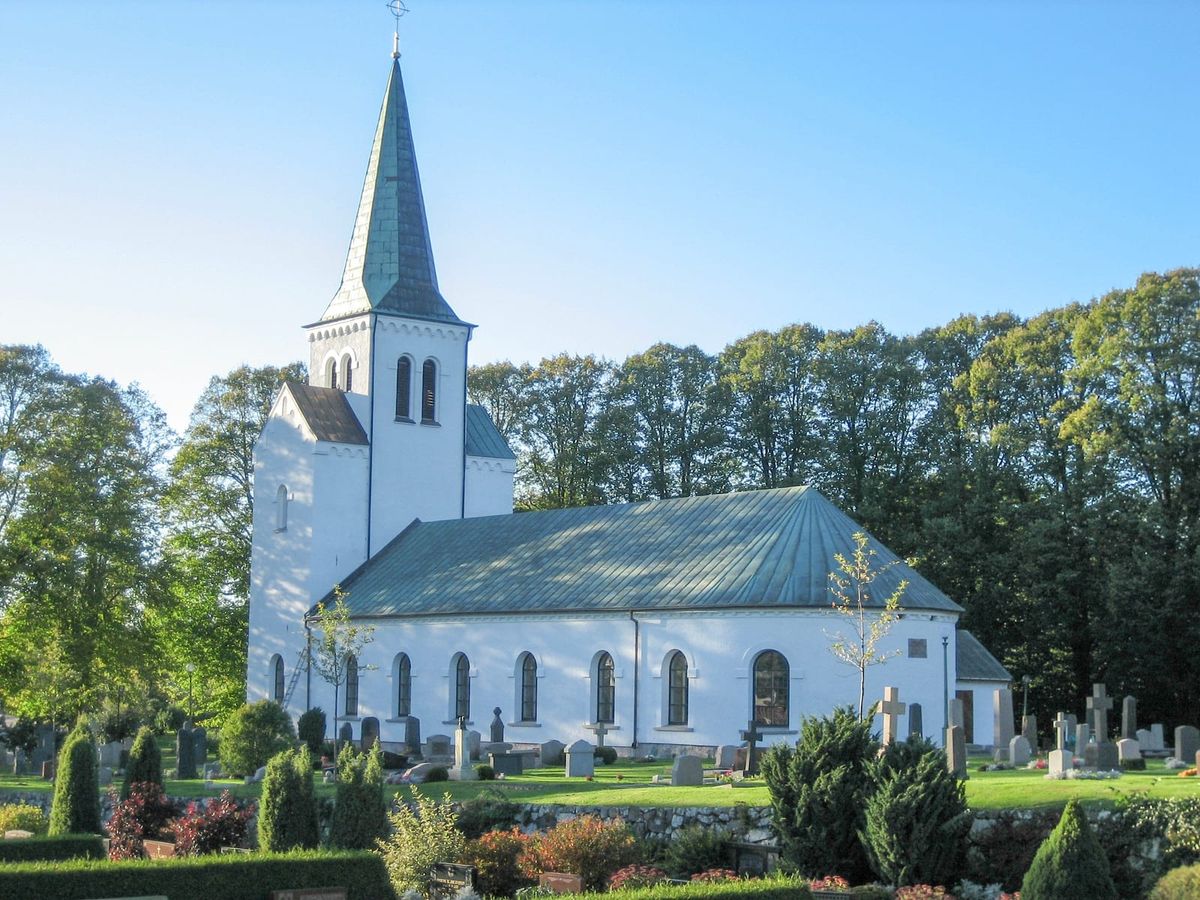 Getinge kyrka med vita murar och grön kopparspira, och kyrkogården en klar höstkväll