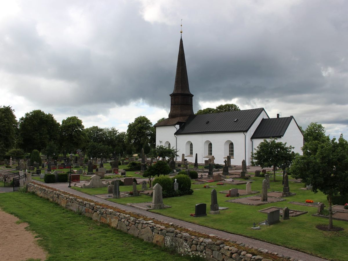 Söndrums kyrka med vit fasad och mörk spånklädd tornspira, sedd över kyrkogården i västra Halmstad